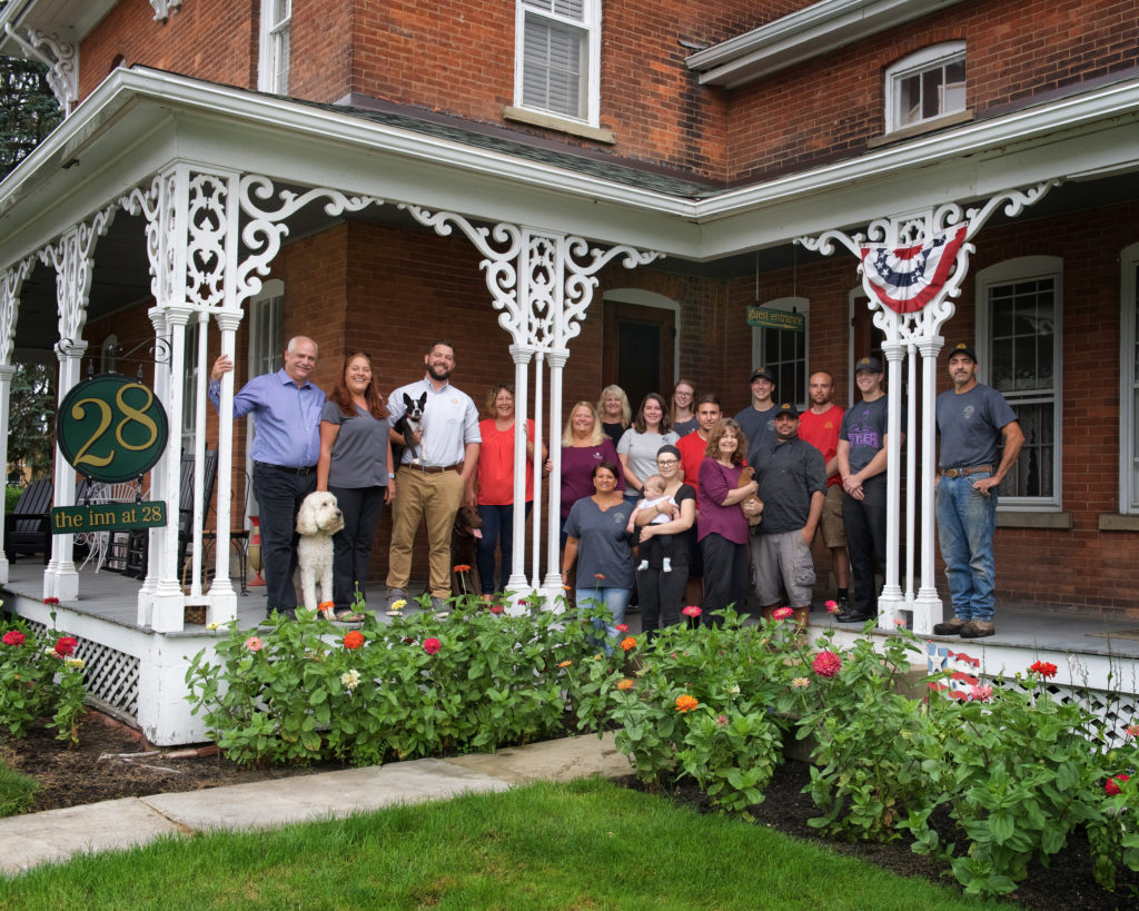 Several people standing on porch of large brick building with flowers in front