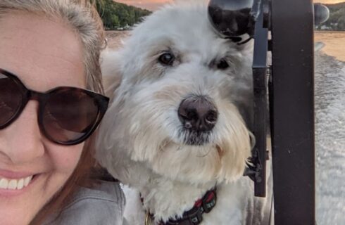 A woman in sunglasses with her white dog on a boat on a lake
