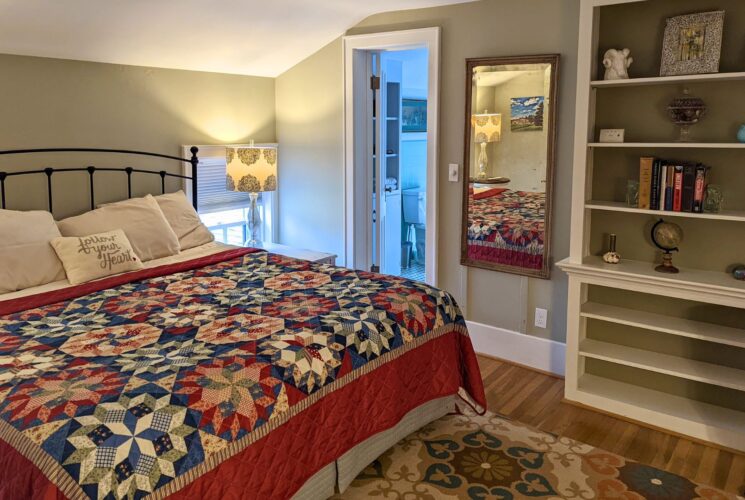 Cozy bedroom with queen bed with colorful quilt, built in bookshelves and attached bathroom