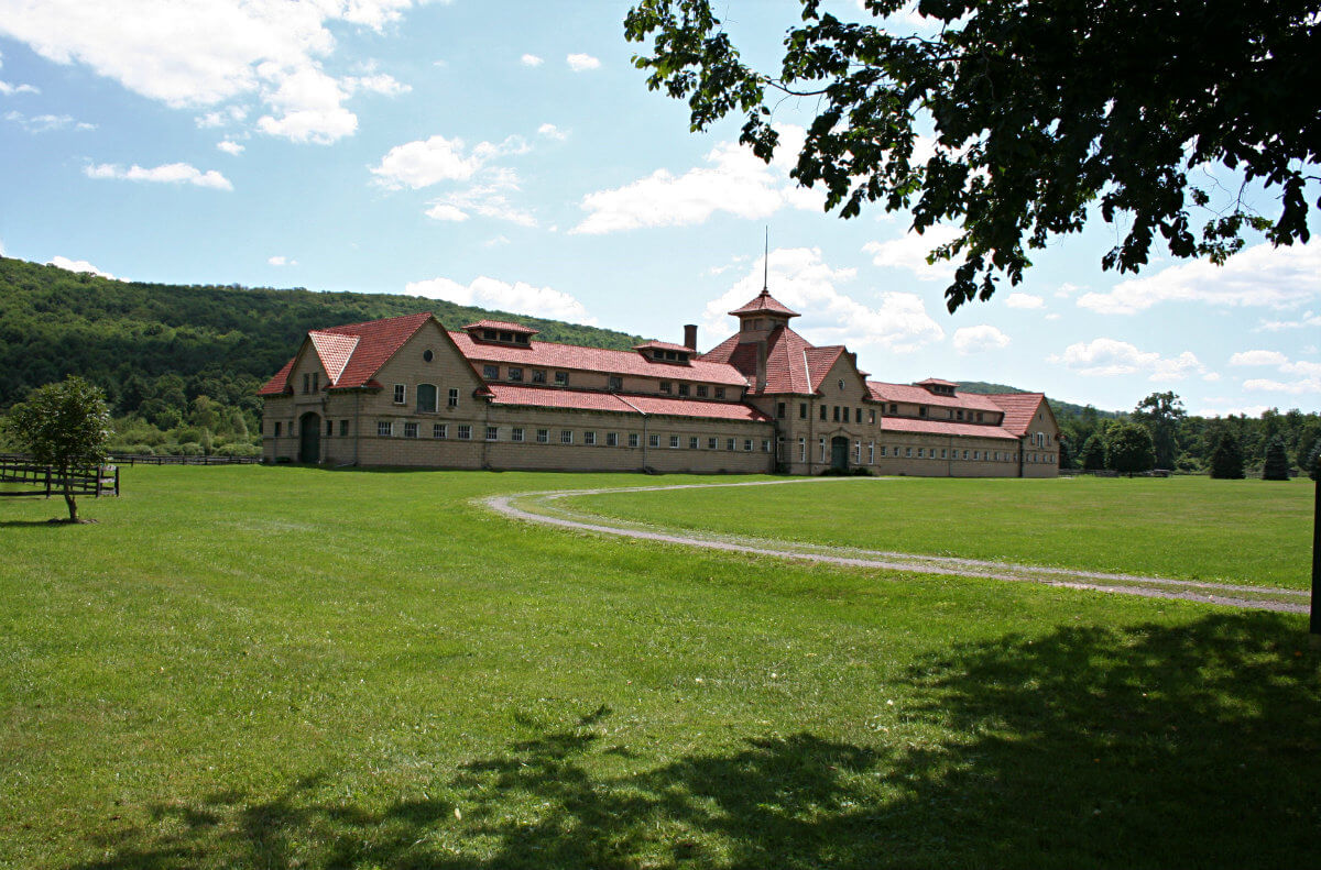 Extra-large, tab stone block barn with red roof in blue sky and green grass scenery