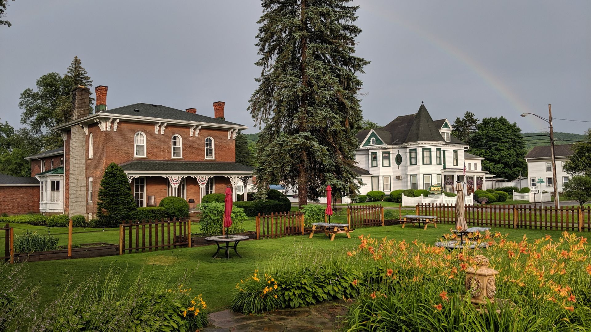 Row of stately houses next to a large open garden and lawn space with picnic tables and lush flowerbeds