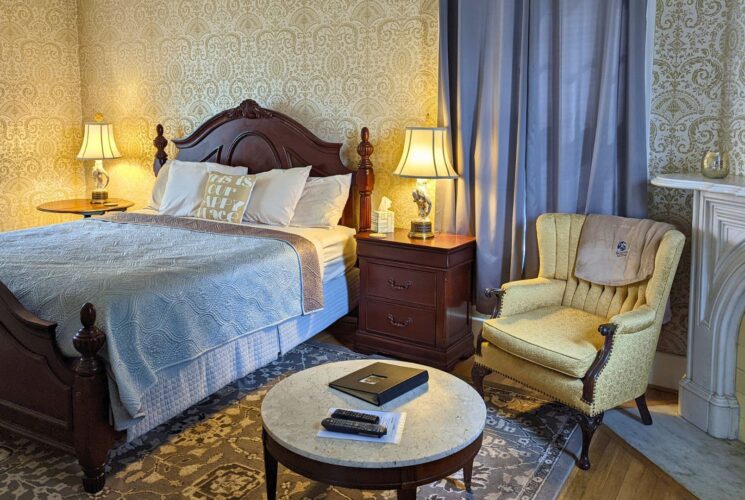 Elegant bedroom with bed with dark wood headboard and footboard, sitting chair and table by fireplace and decorative wallpaper