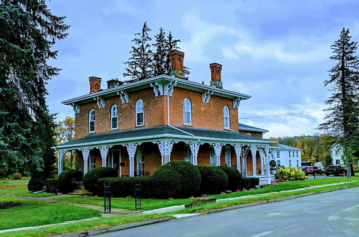 Outside of an inn with brown brick, white pillars, and green shrubs around the perimeter