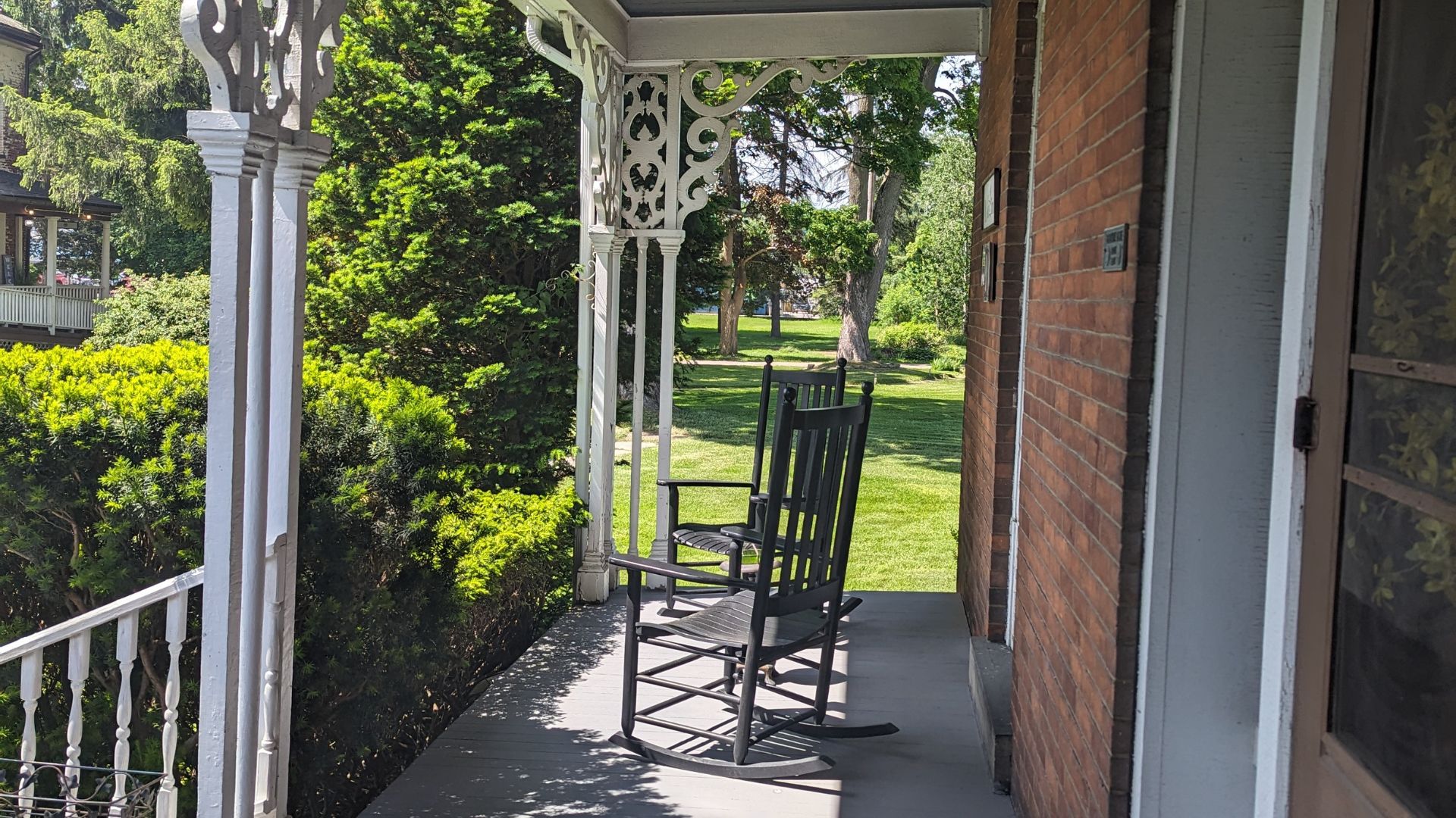 Outdoor patio of a brick home with two black rocking chairs overlooking a lush green yard with grass and trees