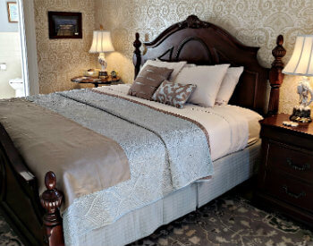 Bedroom with beautiful gold and white wallpaper, deep brown bed and night stands with white bathroom in background