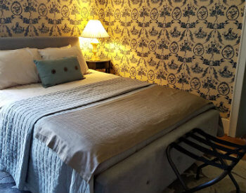 Bedroom with blue and white wallpaper, nightstand with bright light and a black luggage holder at the end of the bed