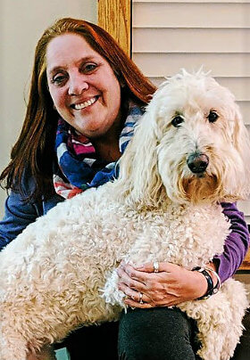 Smiling woman with blue and white scarf holding a large, white dog