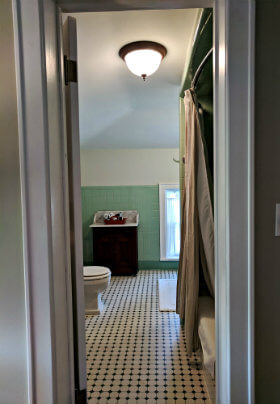 Bathroom with green wall with green and white, patterned floor tiles a bright light fixture