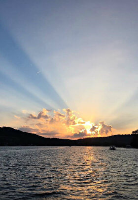 Wavy lake, black silhouette hills with beautiful yellow sunset, sun rays and blue sky in the background