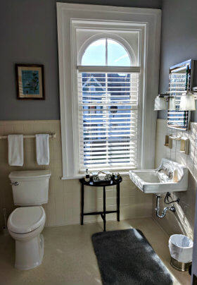 White bathroom with white fixtures, grey bathmat and a large arched window