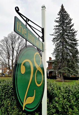 Green and gold sign with tall, pine tree and large, red brick home in the background