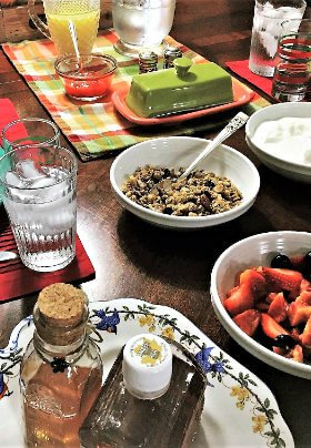 Brown table set with yogurt, strawberries, blueberries, granola in white dishes plus jelly, honey and maple syrup