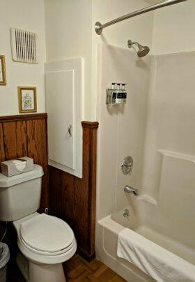 Bathroom with half white, half brown paneled walls and white toilet and shower