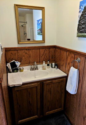Brown vanity with white countertop, a mirror and half white, half brown paneled walls