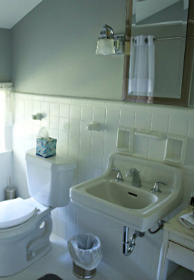 Bathroom with white toilet and sink, a mirror and white tile and green walls