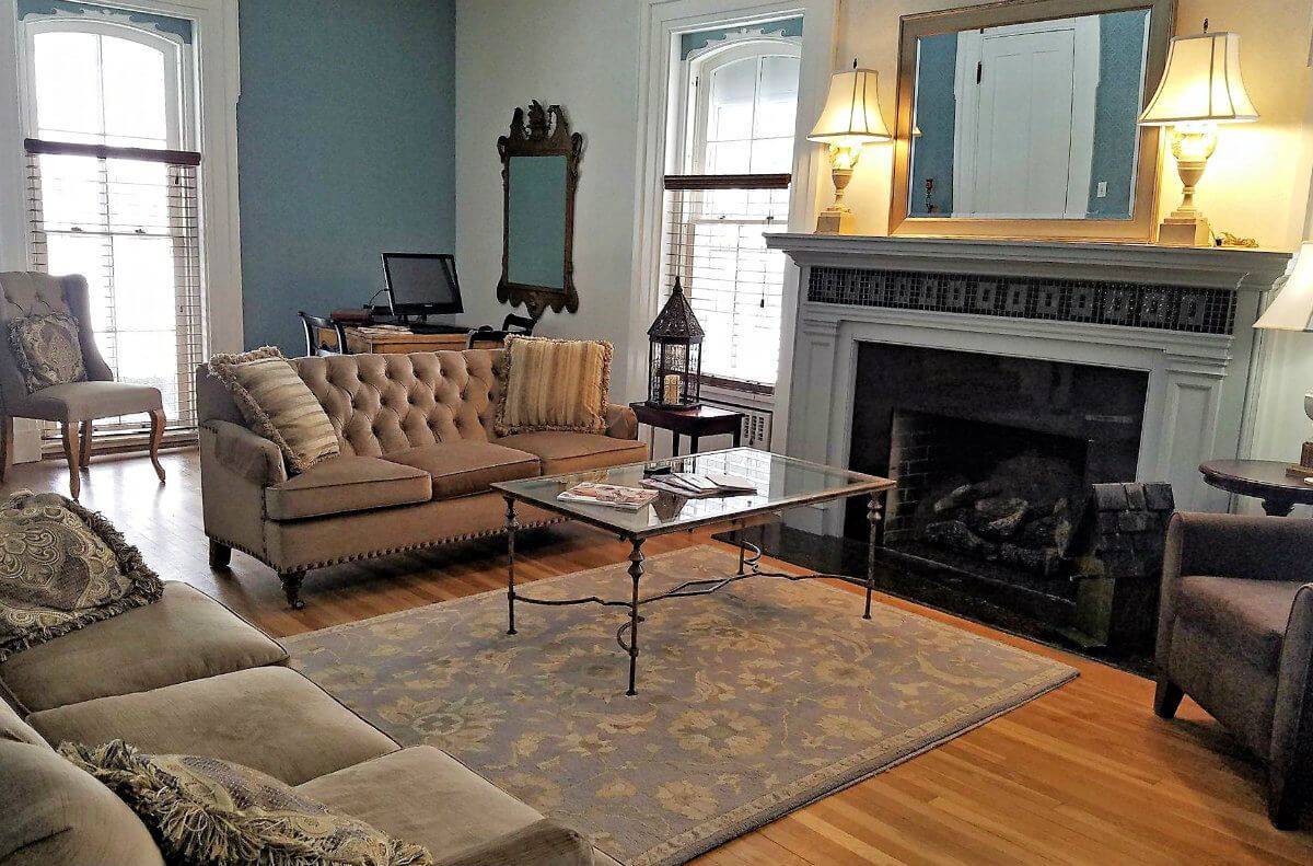 Beautiful blue and white living room with two tan couches, a brown chair and a detailed white fireplace