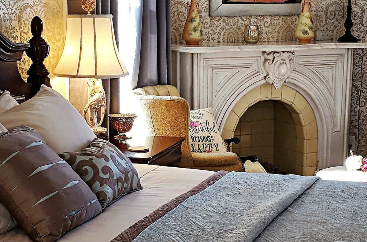 Elegant bedroom with light blue and cream-colored bedding, an ornate fireplace and seating area